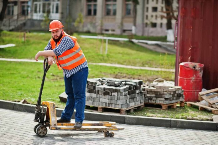 barba-brutale-lavoratore-uomo-vestito-operaio-edile-in-casco-arancione-di-sicurezza-con-transpallet